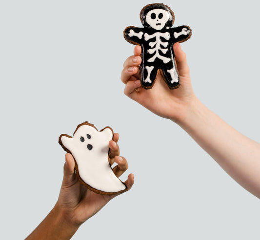 Two hands holding a cute skeleton and ghost cookie.