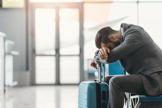 Man in an airport resting his forehead on the handle of his suitcase